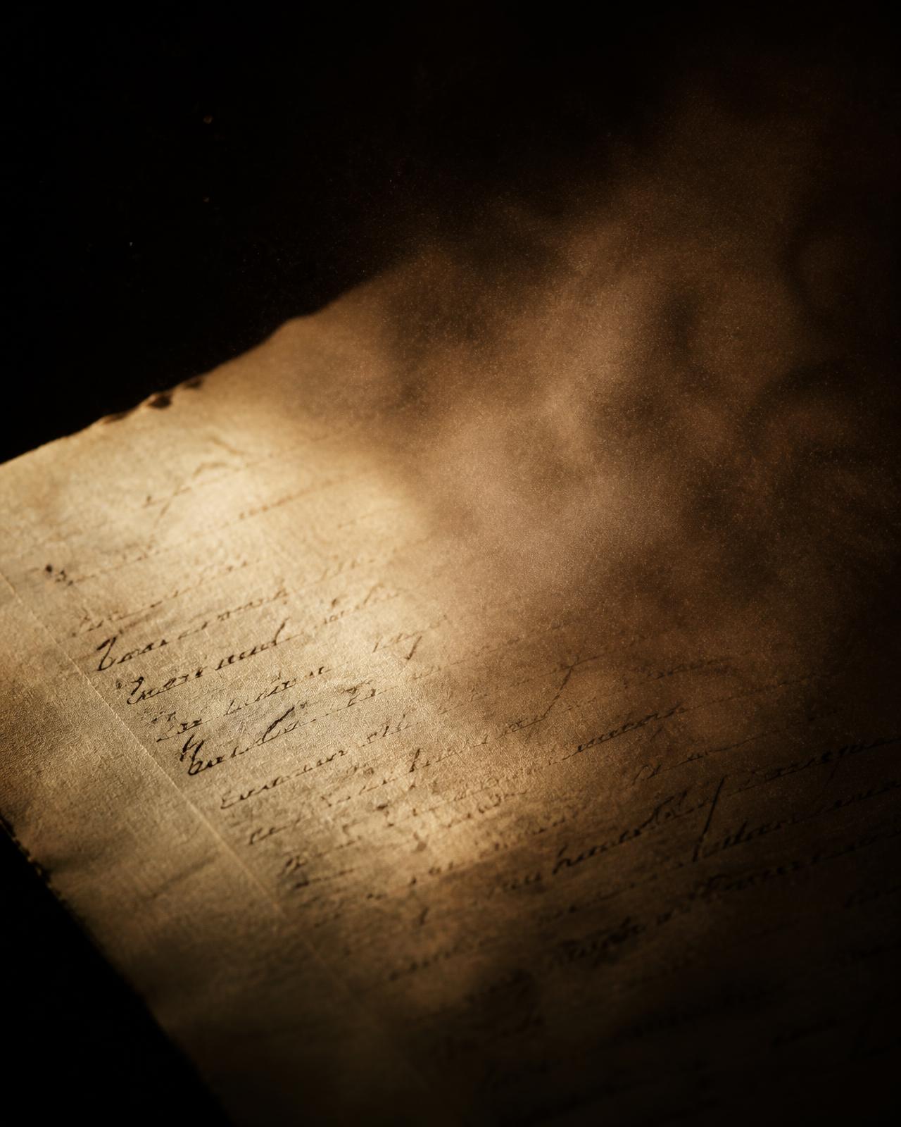 Handwritten manuscript page lit by warm raking light against near-black